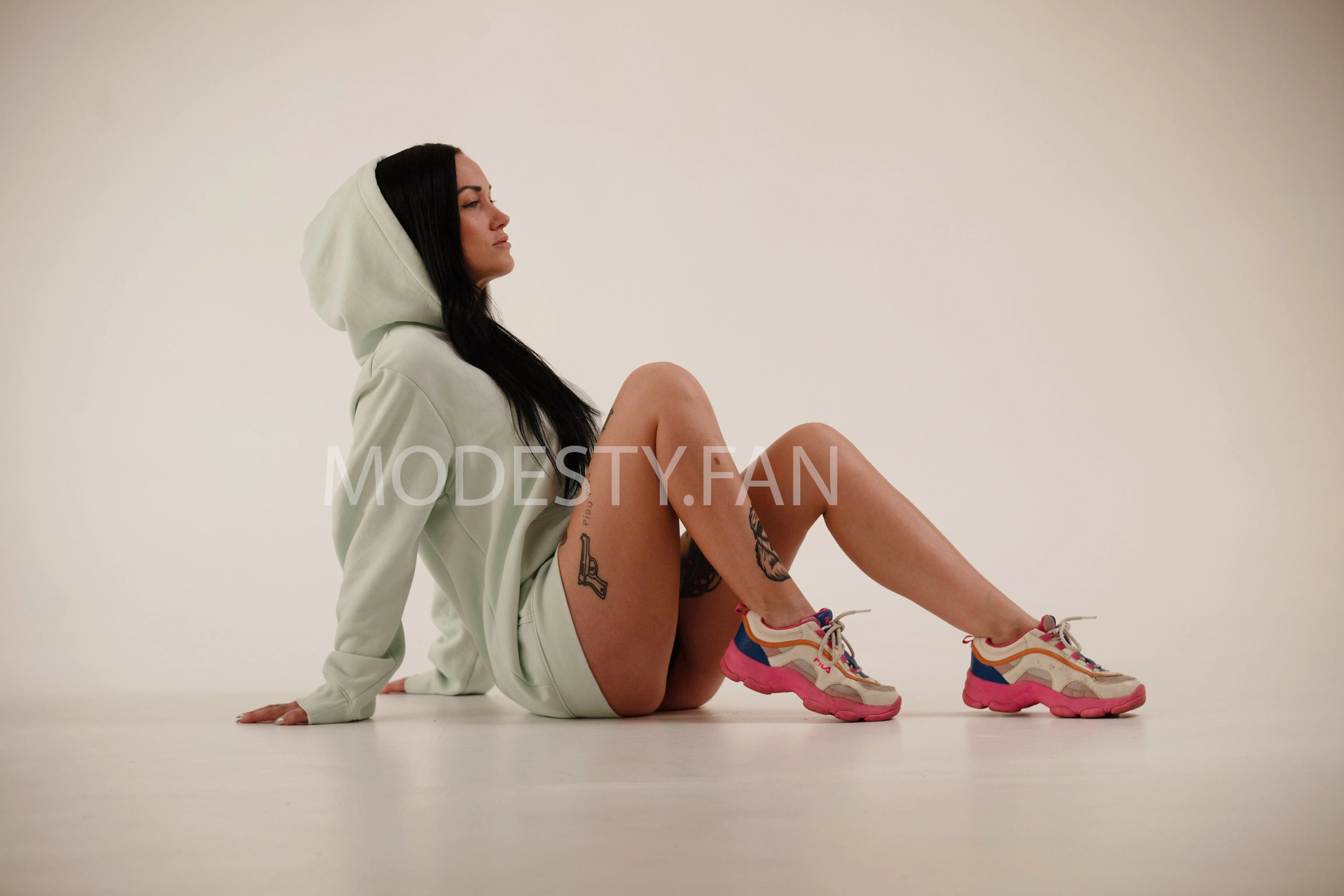 Petite brunette wearing a hoodie showing off her arm tattoos